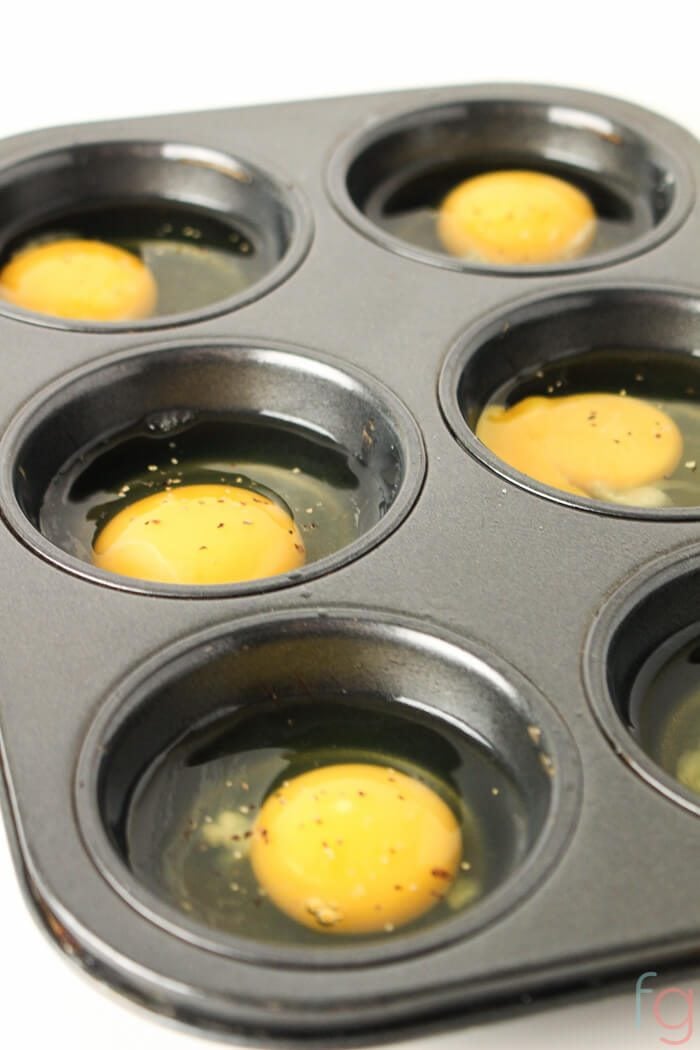 muffin tin with cracked eggs and a bit of pepper