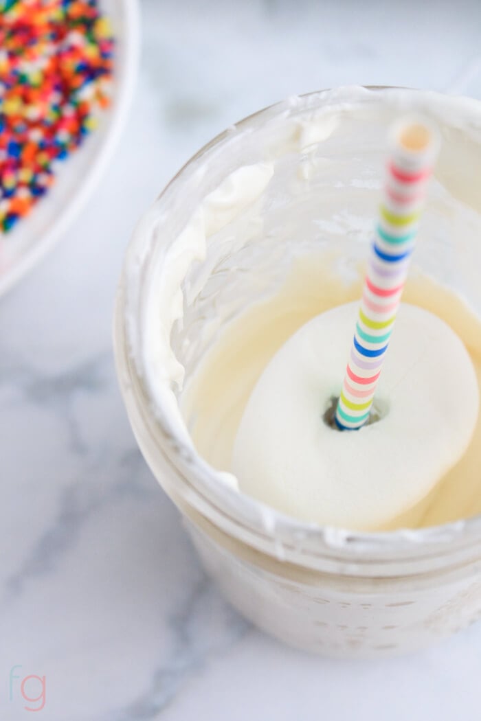 dipping a marshmallow pop in melted white chocolate.