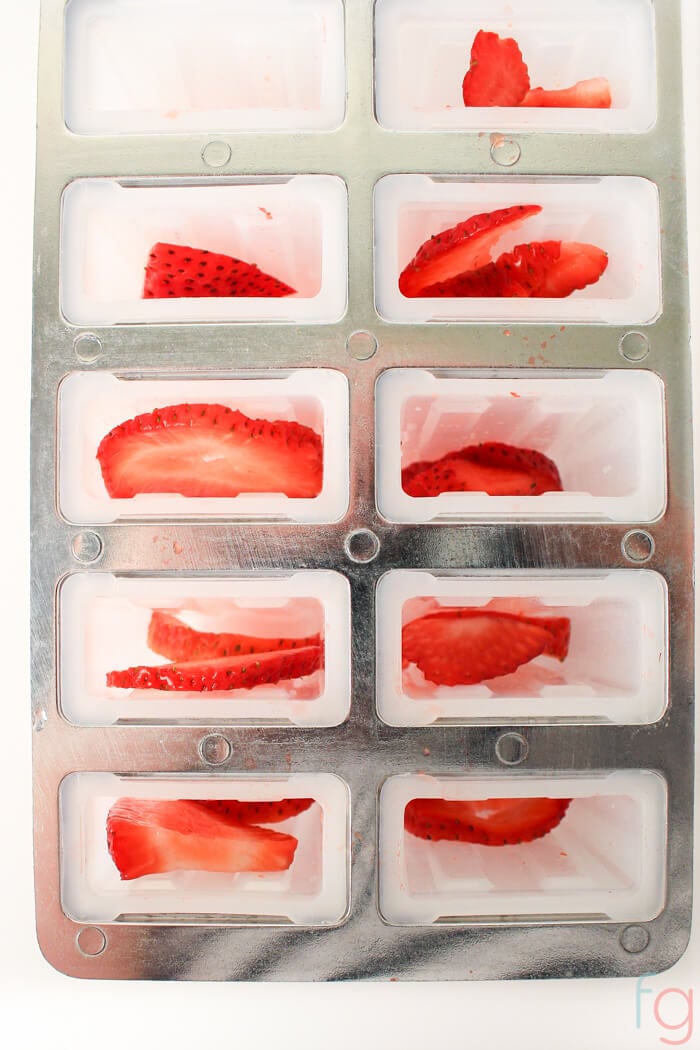 Distributing sliced strawberries in the popsicle molds.