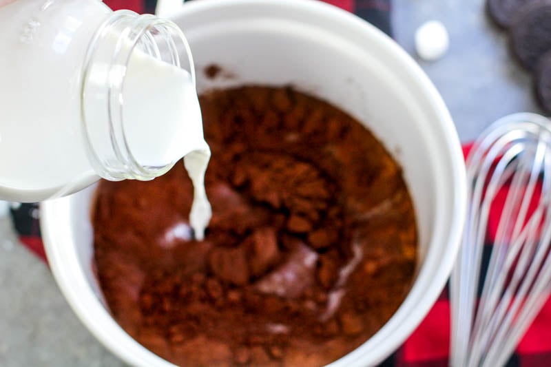 Milk being poured slowly into hot cocoa powder.