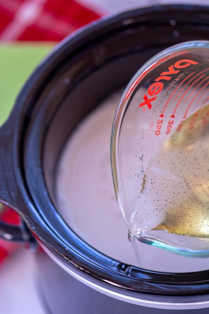 measuring cup filled with simple syrup adding to the crock pot.