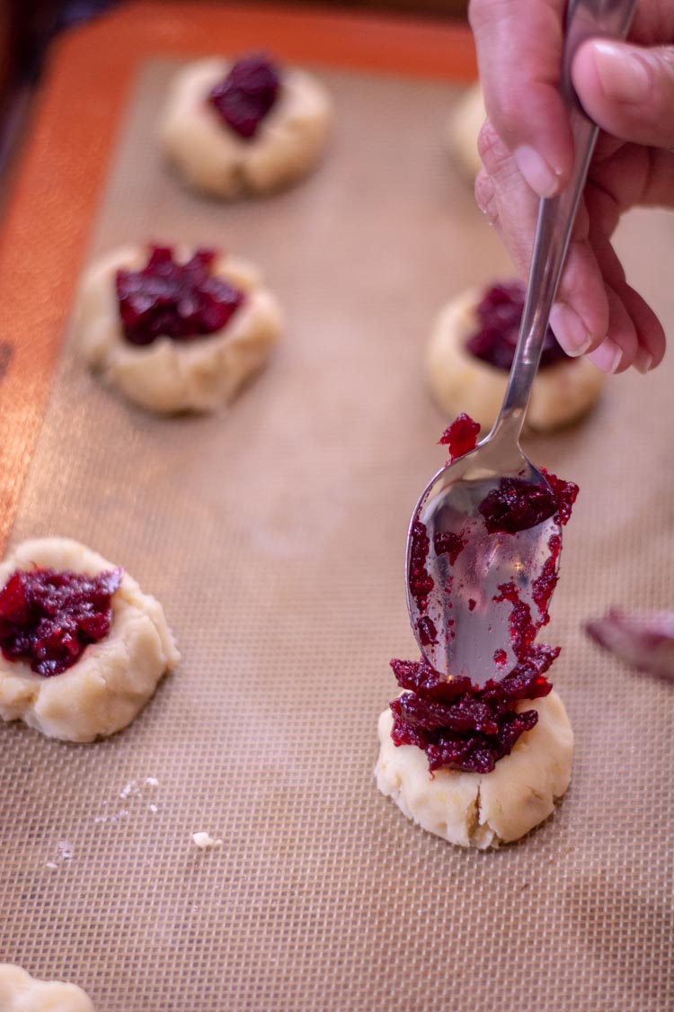 Closeup of the cookie with jam and a spoon to fill the thumbprint.