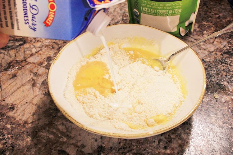 pouring milk into a white bowl to form the waffle batter.