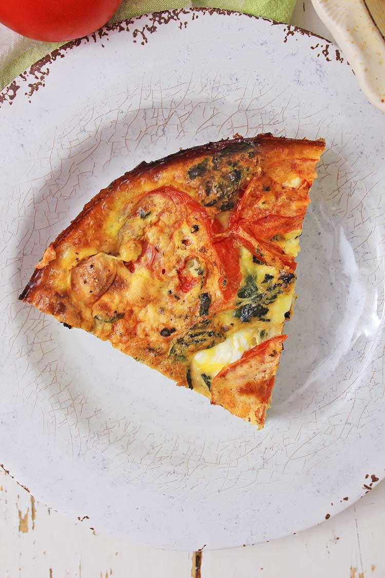 top down view of a slice of crustless caprese quiche on a white serving plate.