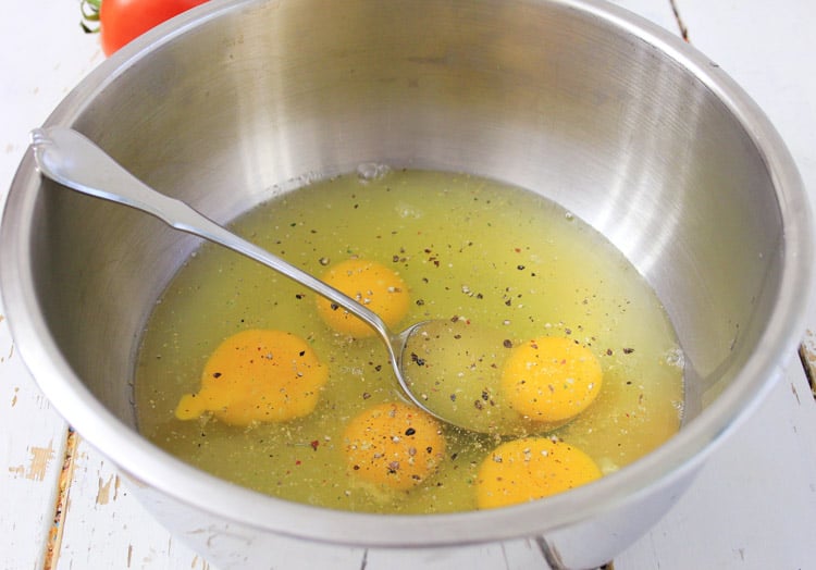 Salt and Pepper in the egg mixture with a silver spoon in a silver mixing bowl.