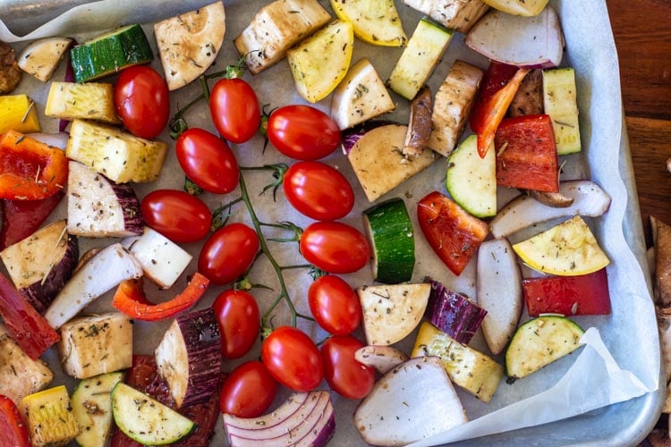 top down view of a sheet pan with parchment paper and lightly oiled vegetables ready to go into the oven.