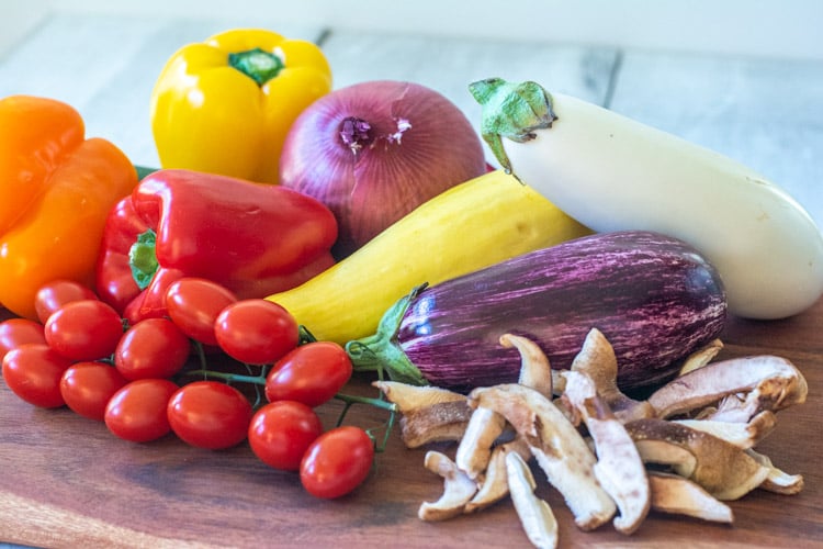 Several different vegetables on a wooden cutting board ready to be made into a sheet pan roasting.