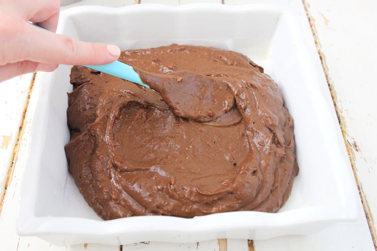 Spreading the brownie batter in a white baking dish.