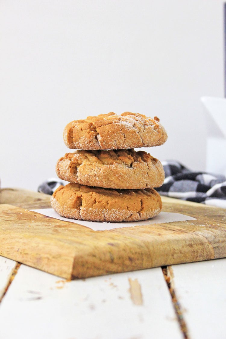 three gluten free peanut butter cookies stacked on a cutting board.