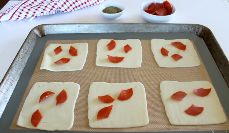 fresh slices of mozzarella cheese on a lined sheet pan with pepperoni slices ready to go in the oven.