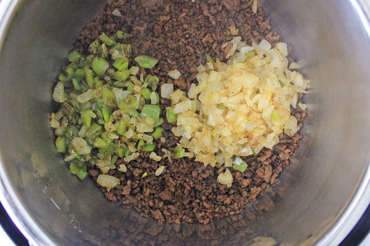 adding the sautéed onions and green peppers on top of the ground beef.