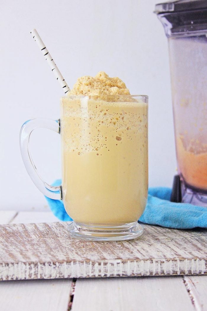 glass mug on white board filled with ice cold Frappuccino and the mixer in the background.