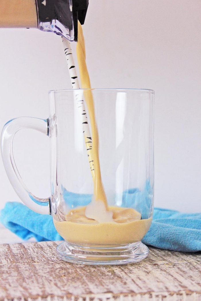 pouring Frappuccino into a clear glass mug with a fun black and white straw.