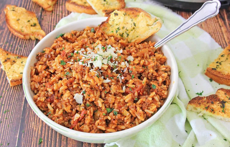 Lots of garlic bread spread along the table surrounding the bowl of spanish rice.