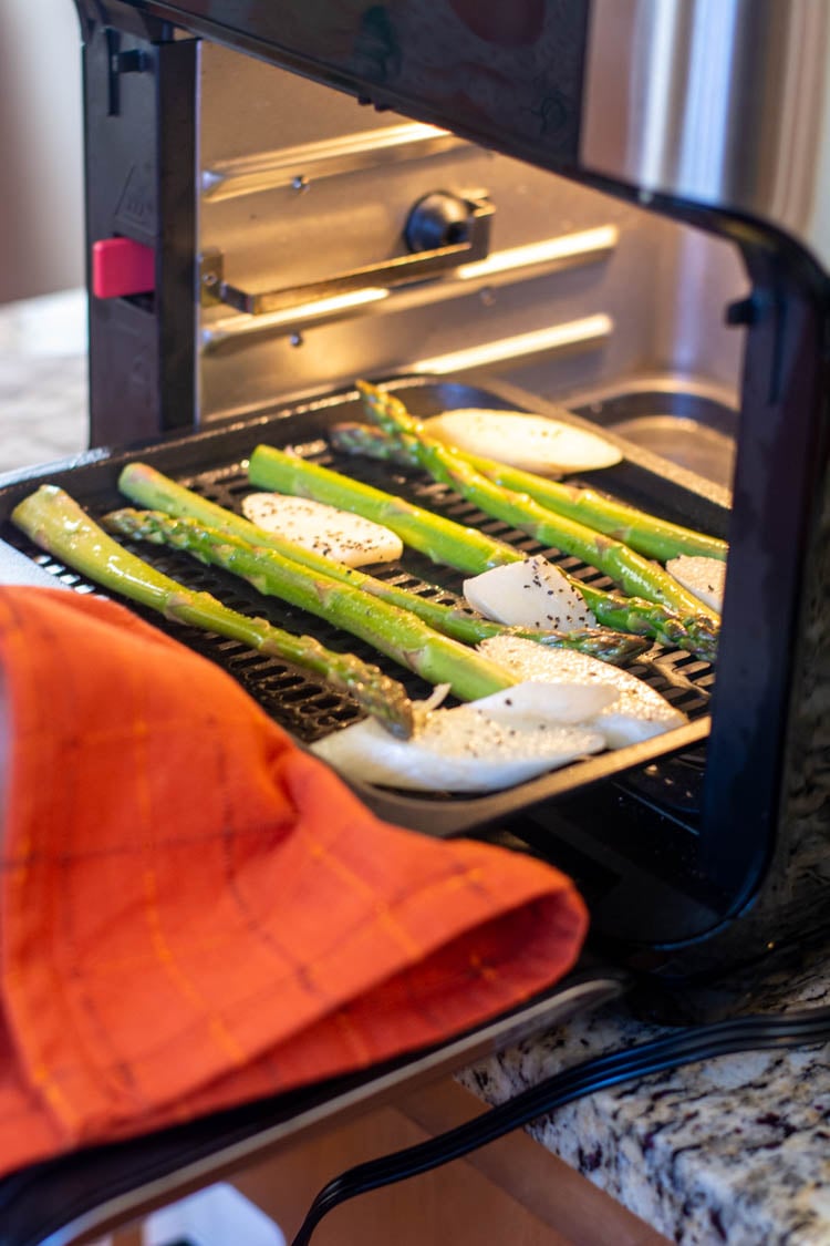 inserting the tray with asparagus into the middle shelf of the air fryer.