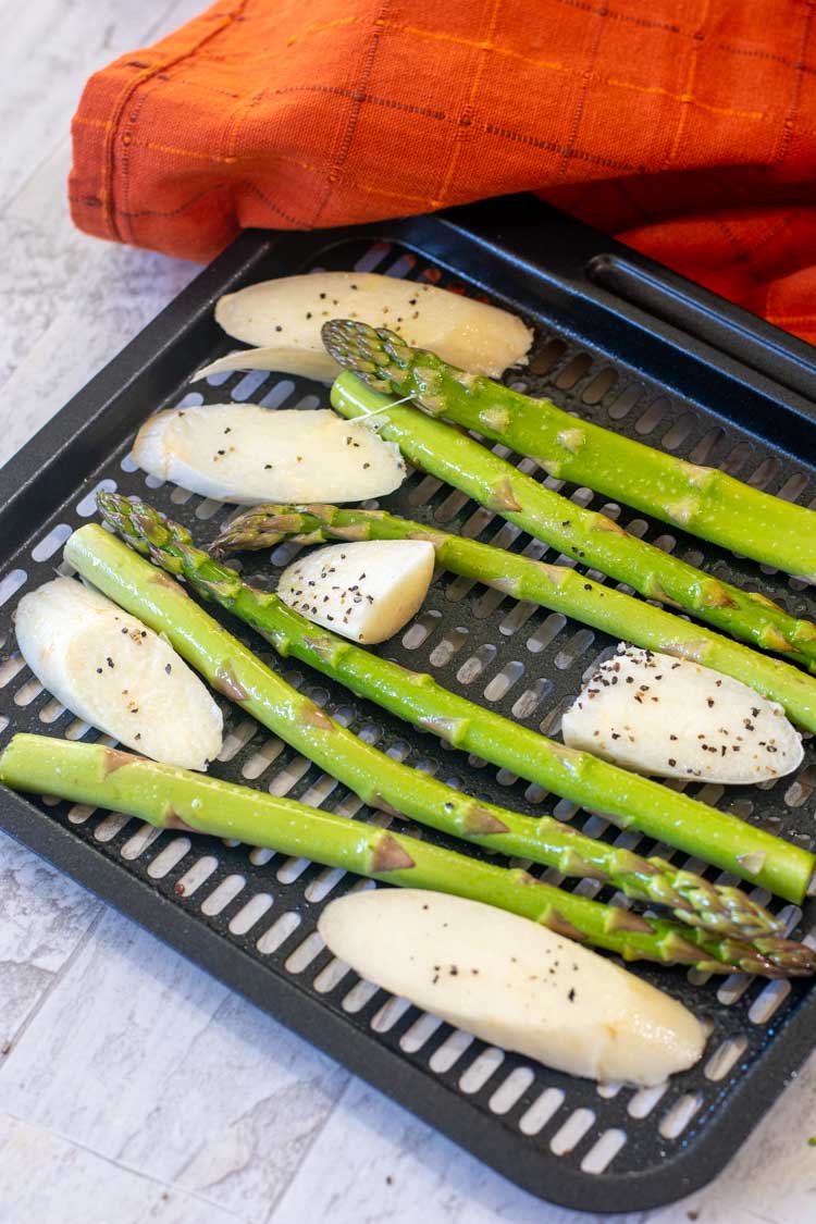 air fryer tray with green asparagus spears and sliced white asparagus coated with a bit of salt and pepper.