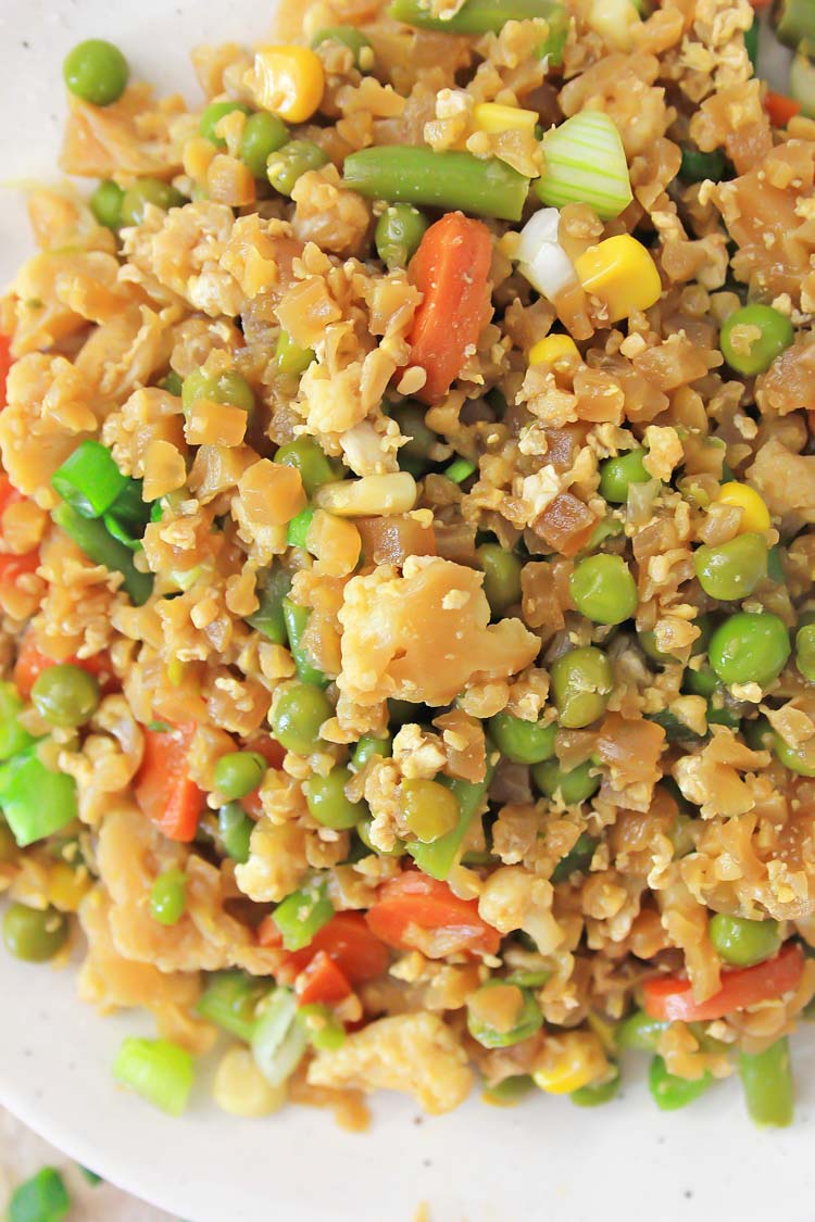 Close-up of cauliflower fried rice with egg and veggies on a white plate.