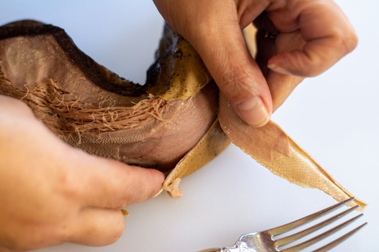 Beef tongue on a white cutting board being peeled.