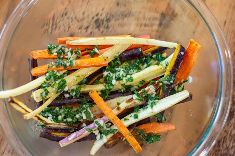 carrot sticks added to a glass bowl with garlic butter and fresh parsley poured on top.