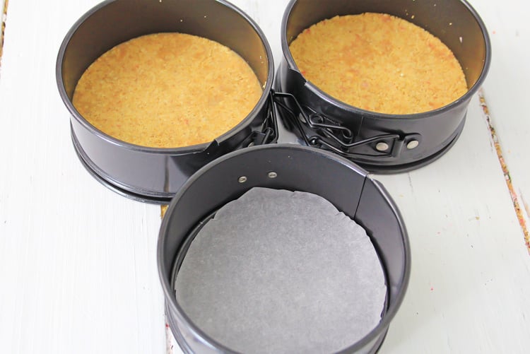 crumbled graham crackers being compressed on a piece of parchment paper inside a springform pan.