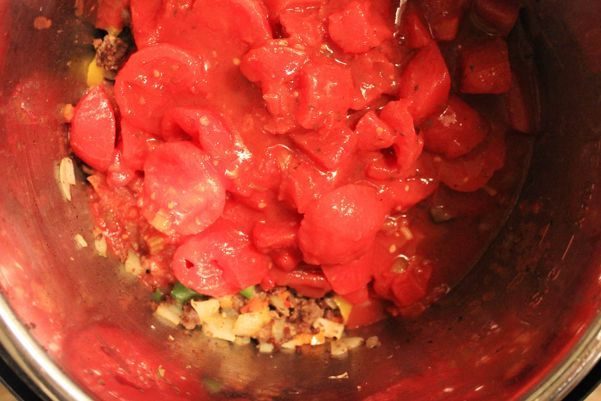 adding the tomatoes to the instant pot over the sautéed onions and beef.