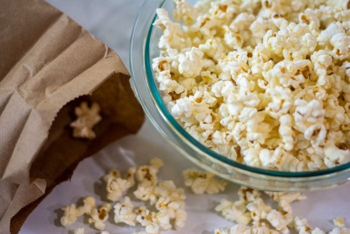 bowl of popcorn and brown lunch bag with open with popped kernels on the table.