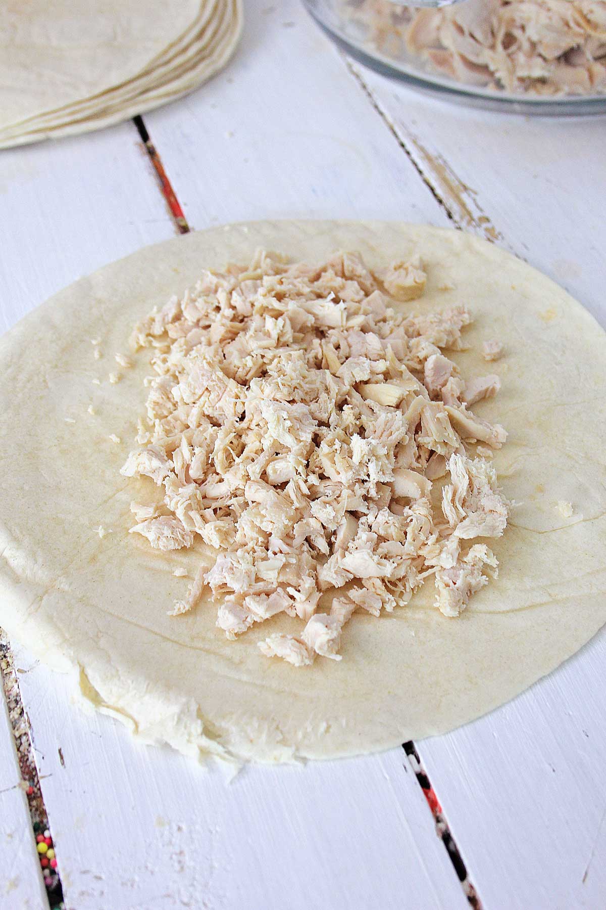 Adding shredded rotisserie chicken to a flour tortilla.