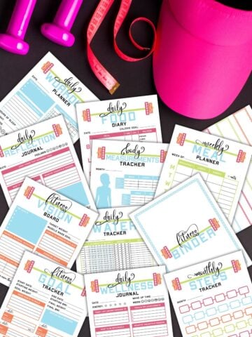Several pages from the printable health and fitness binder next to workout equipment.