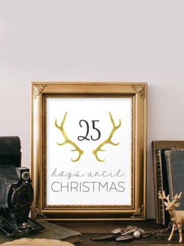 Free printable Christmas countdown wall art in a golden frame, on a wooden desk, next to rustic decor.