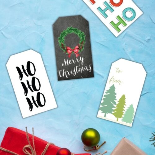 free printable Christmas gift tags on a blue table next to Christmas gifts.