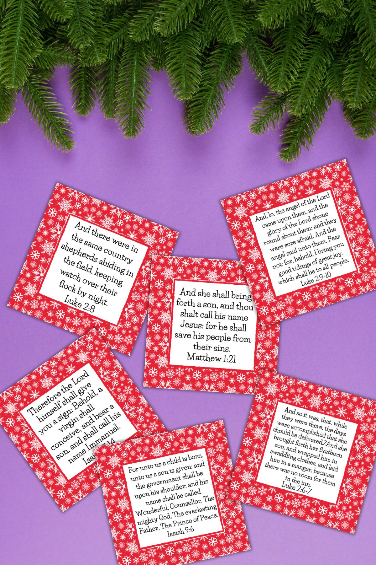 Free printable Bible verse Christmas cards on a purple table next to Christmas tree foliage.