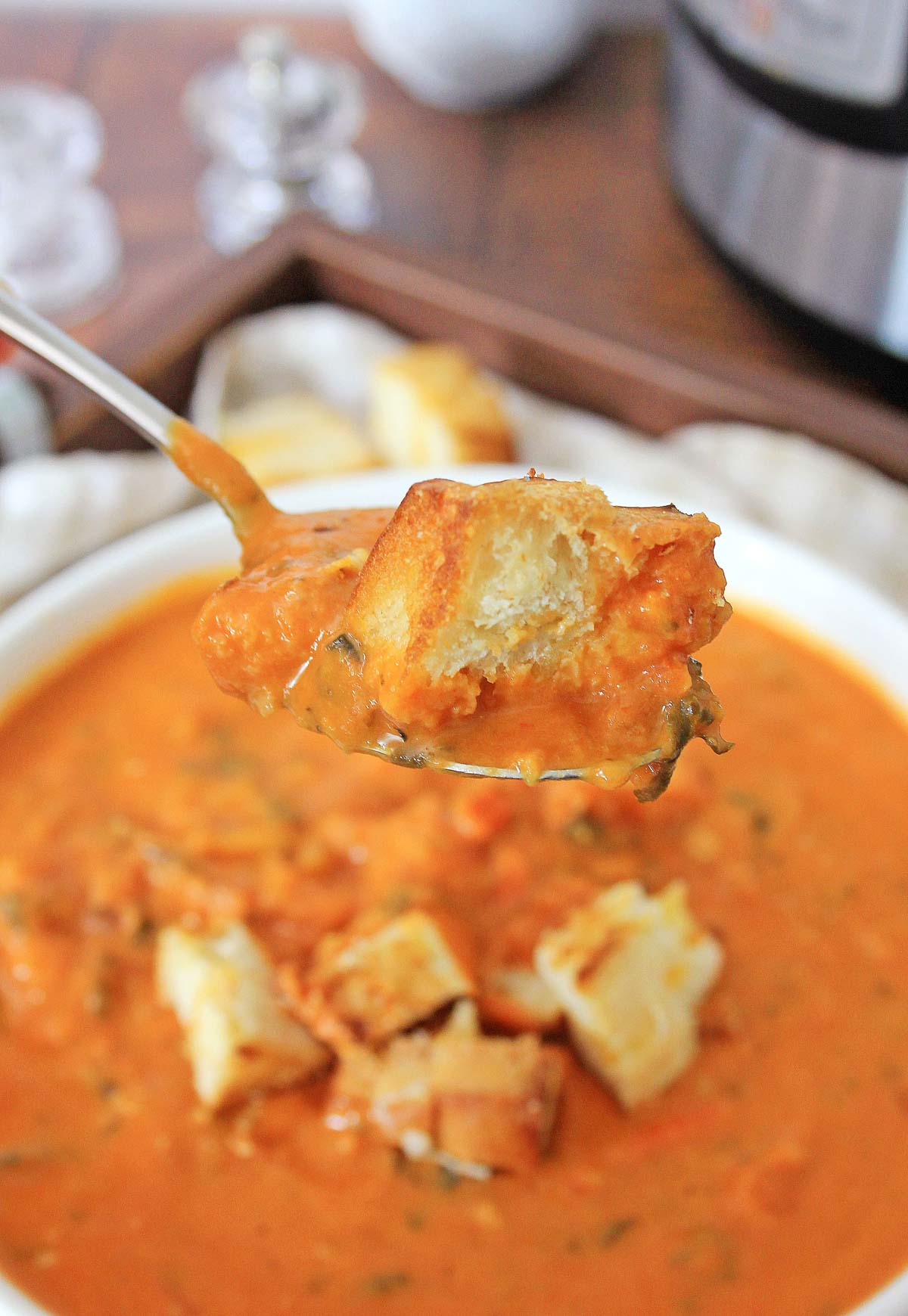 bowl of tomato soup with a spoon full of it and a homemade crouton.