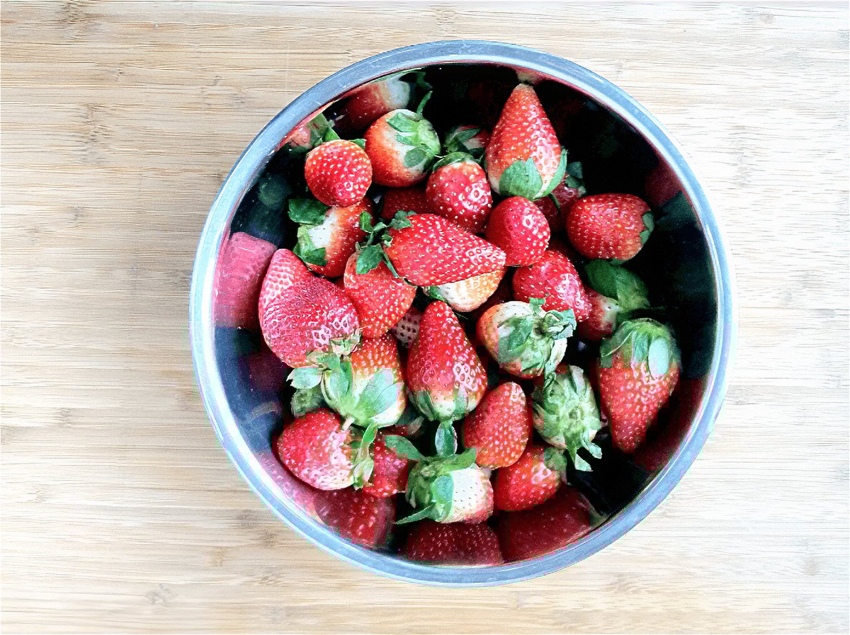 top view of fresh strawberries in a bowl, on a wooden table.