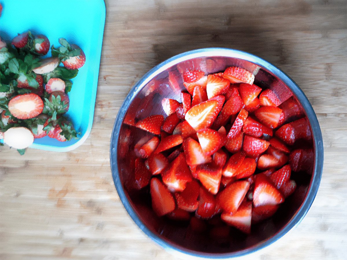 sliced strawberries in a bowl and their leafy tops next to the bowl.
