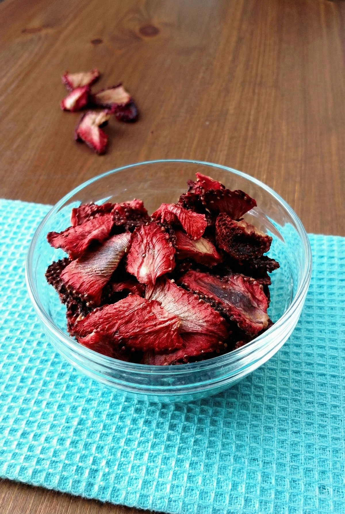 Oven dehydrated strawberries in a glass bowl on a blue kitchen towel.
