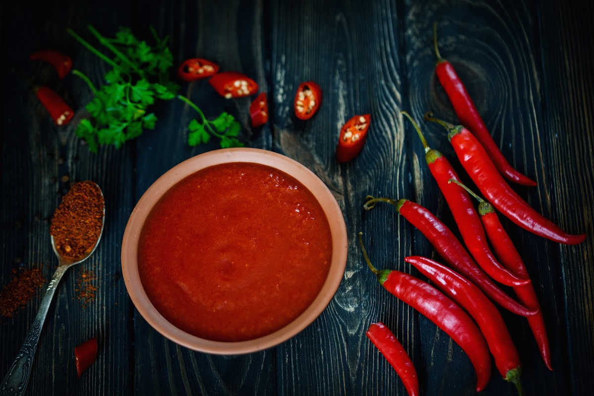 top down view of a bowl of hot sauce with peppers on a black table.
