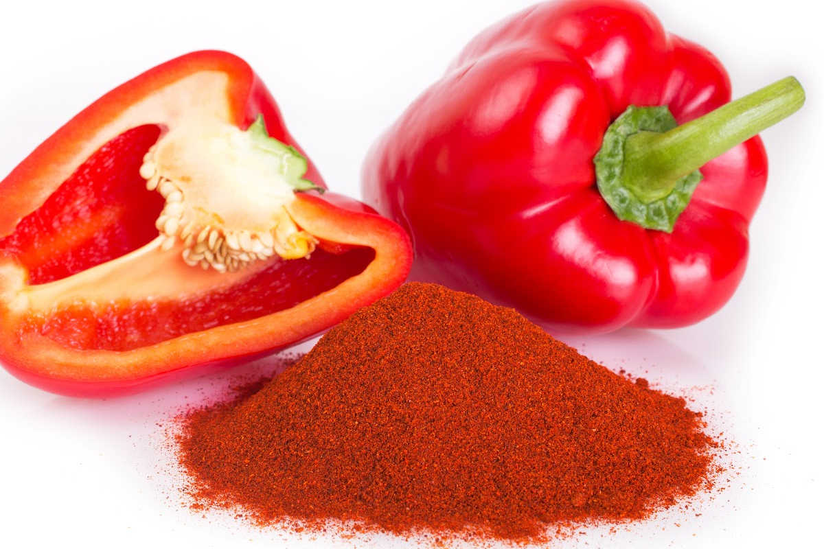 ground paprika in front of two red peppers on a white counter.