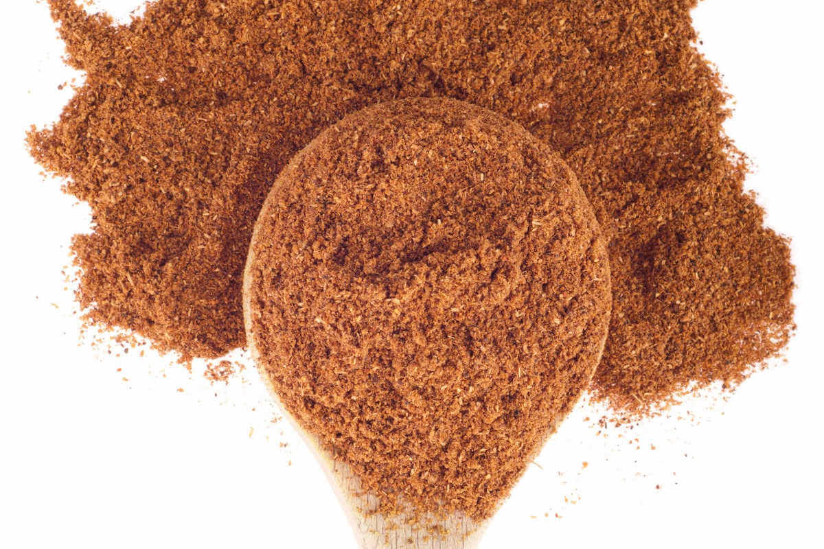 garam masala in its powder form on a spoon with some of the powder spread around the spoon.