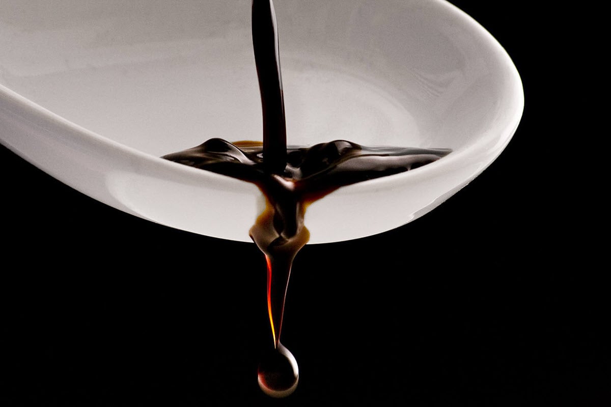 Balsamic vinegar poured in white bowl on black background.