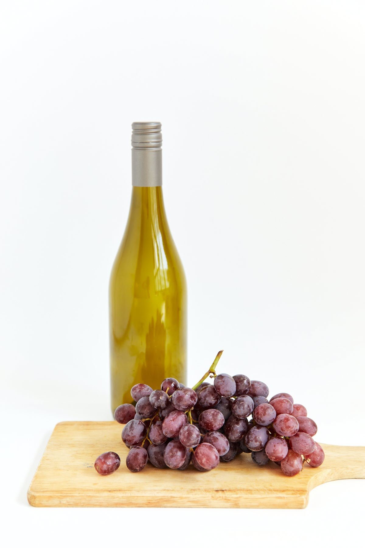 Bottle of white wine vinegar and grapes on wooden cutting board.