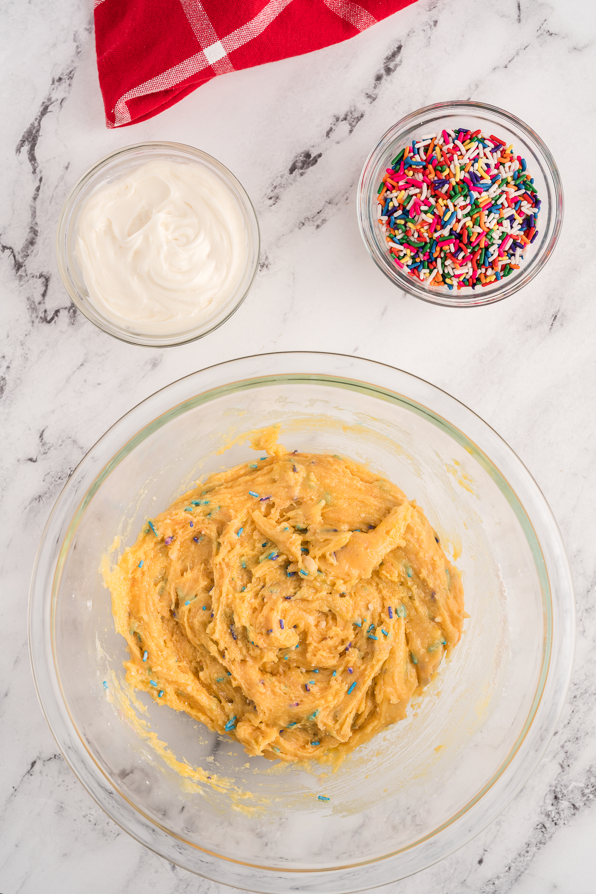 top view of funfetti batter in a bowl, next to smaller bowls with frosting and funfetti.