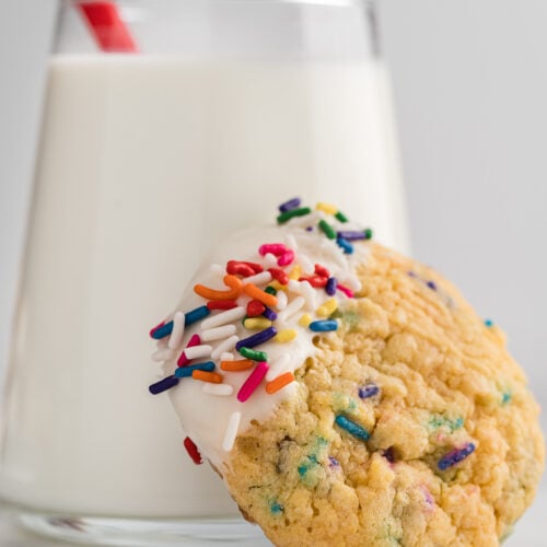 Side view of a homemade funfetti cookie resting on a glass of milk.