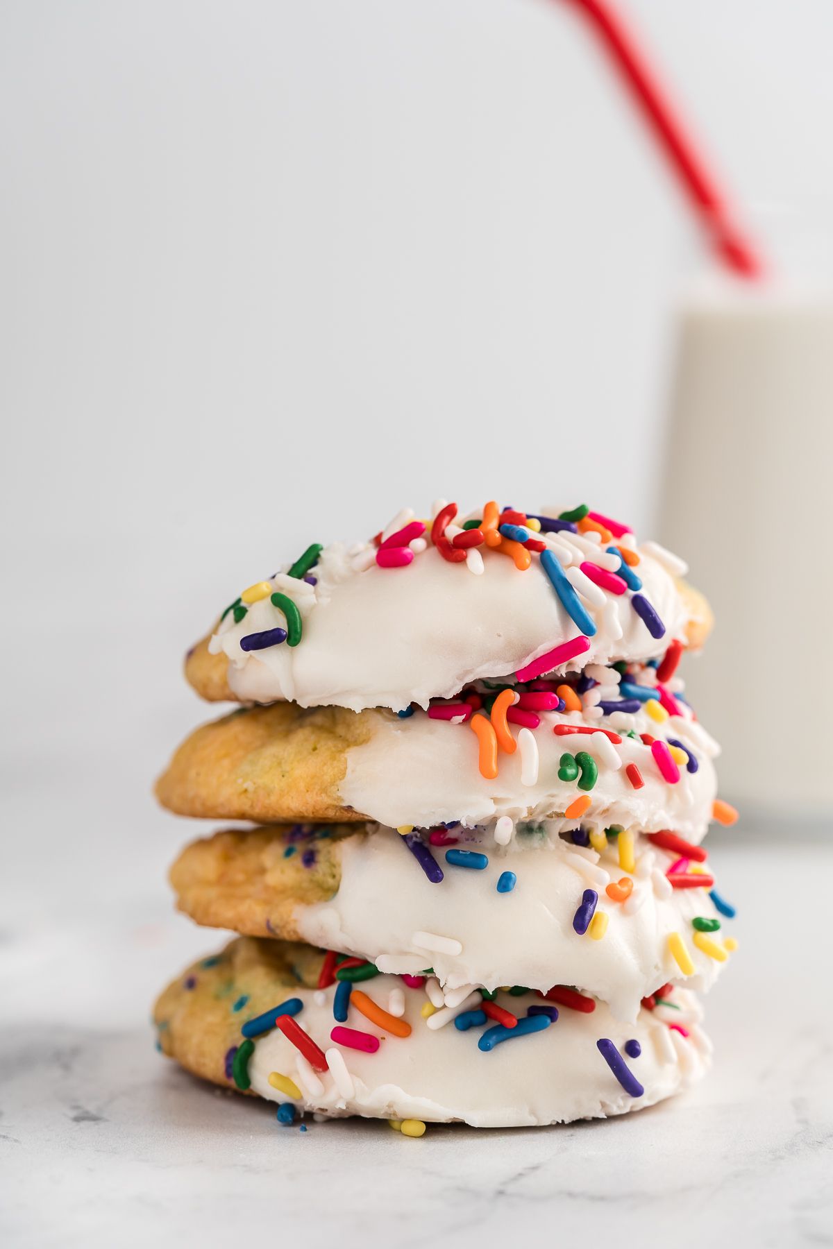 Side view of a stack of funfetti cake mix cookies with a glass of milk in the background.
