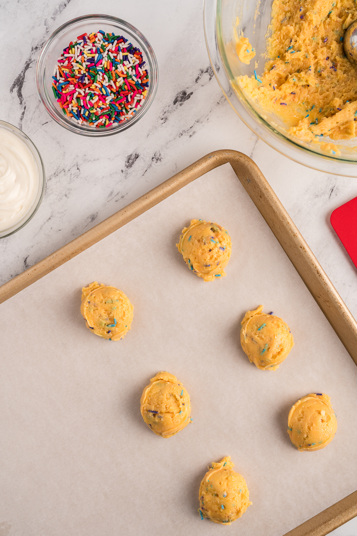 Top view of rolled balls of funfetti cookie dough on a sheet pan