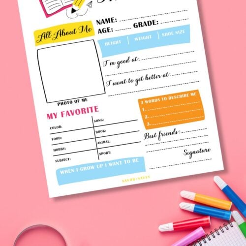 Free printable first day of school interview on pink surface next to colorful school supplies.