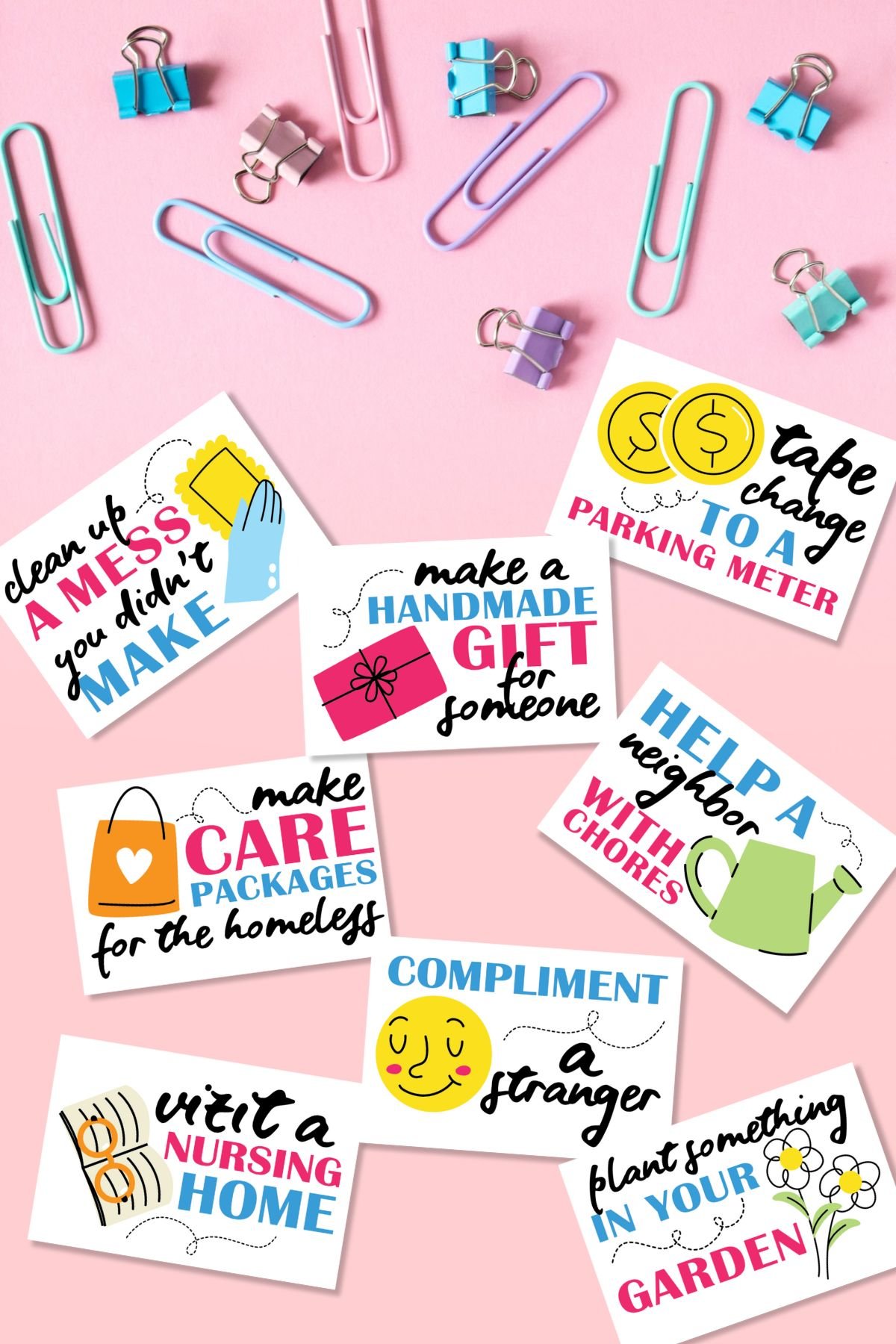 Free printable kindness cards on pink background next to paper clips.