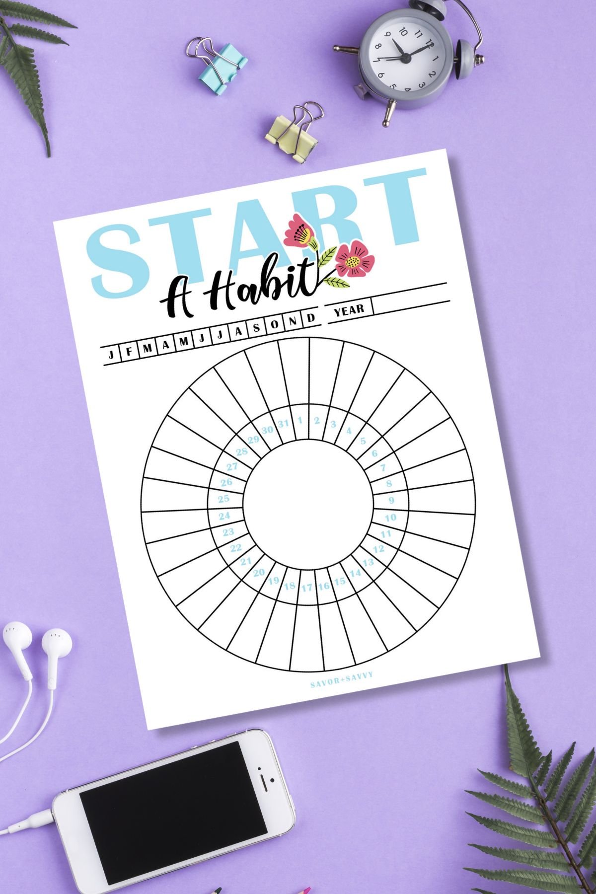 Circular Start A Habit free printable monthly tracker on purple surface next to smartphone, alarm clock, and foliage.
