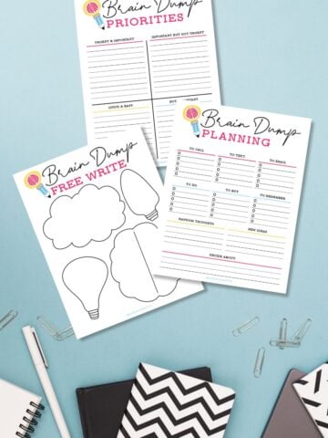 Three free printable brain dump worksheets on a blue surface next to stationery.