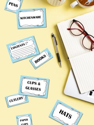 Free printable storage bin labels on yellow surface next to glasses and stationery.