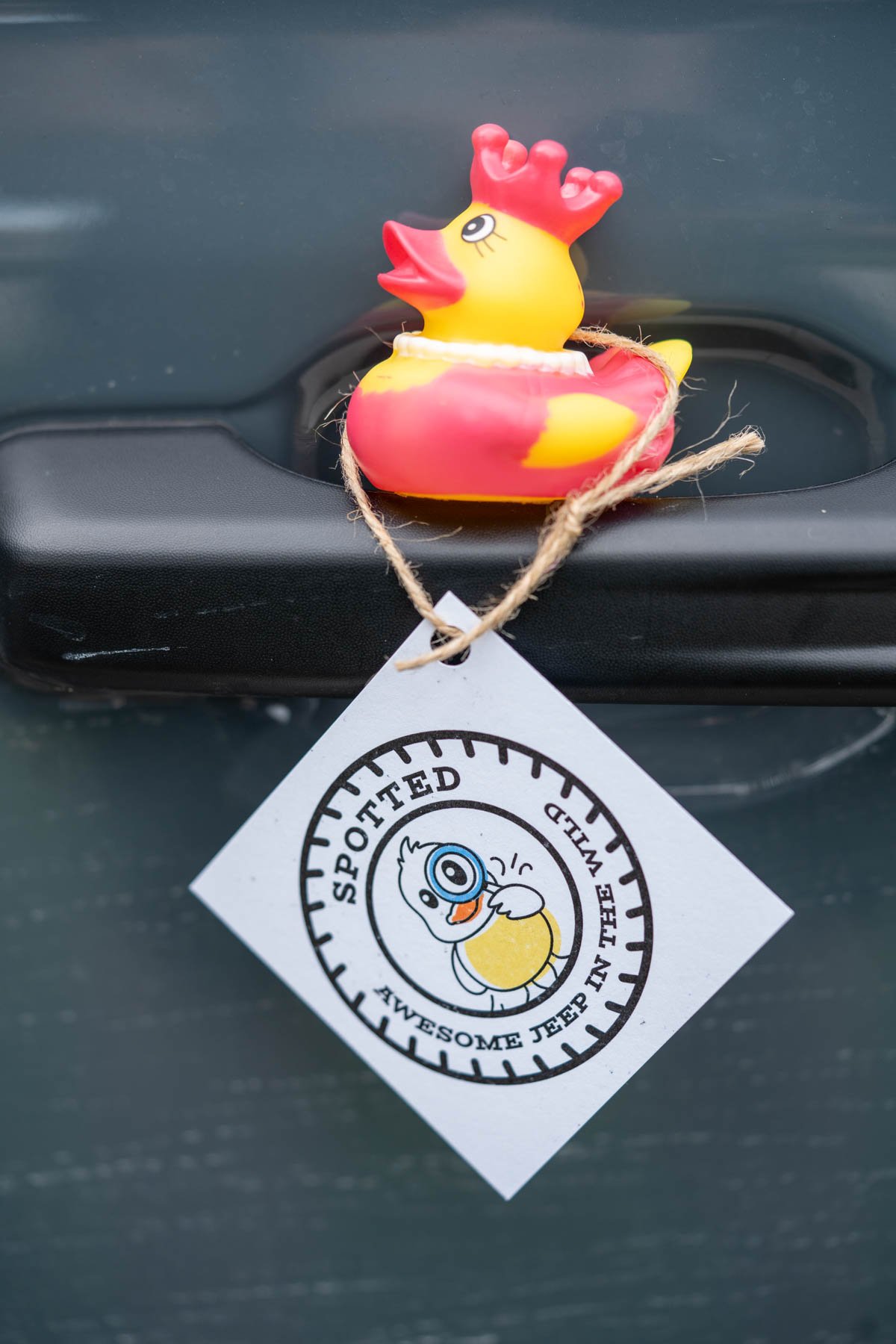A cute rubber duck with a duck duck jeep tag attached that says "Spotted: Awesome Jeep in the wild", sitting on the door handle of a jeep.